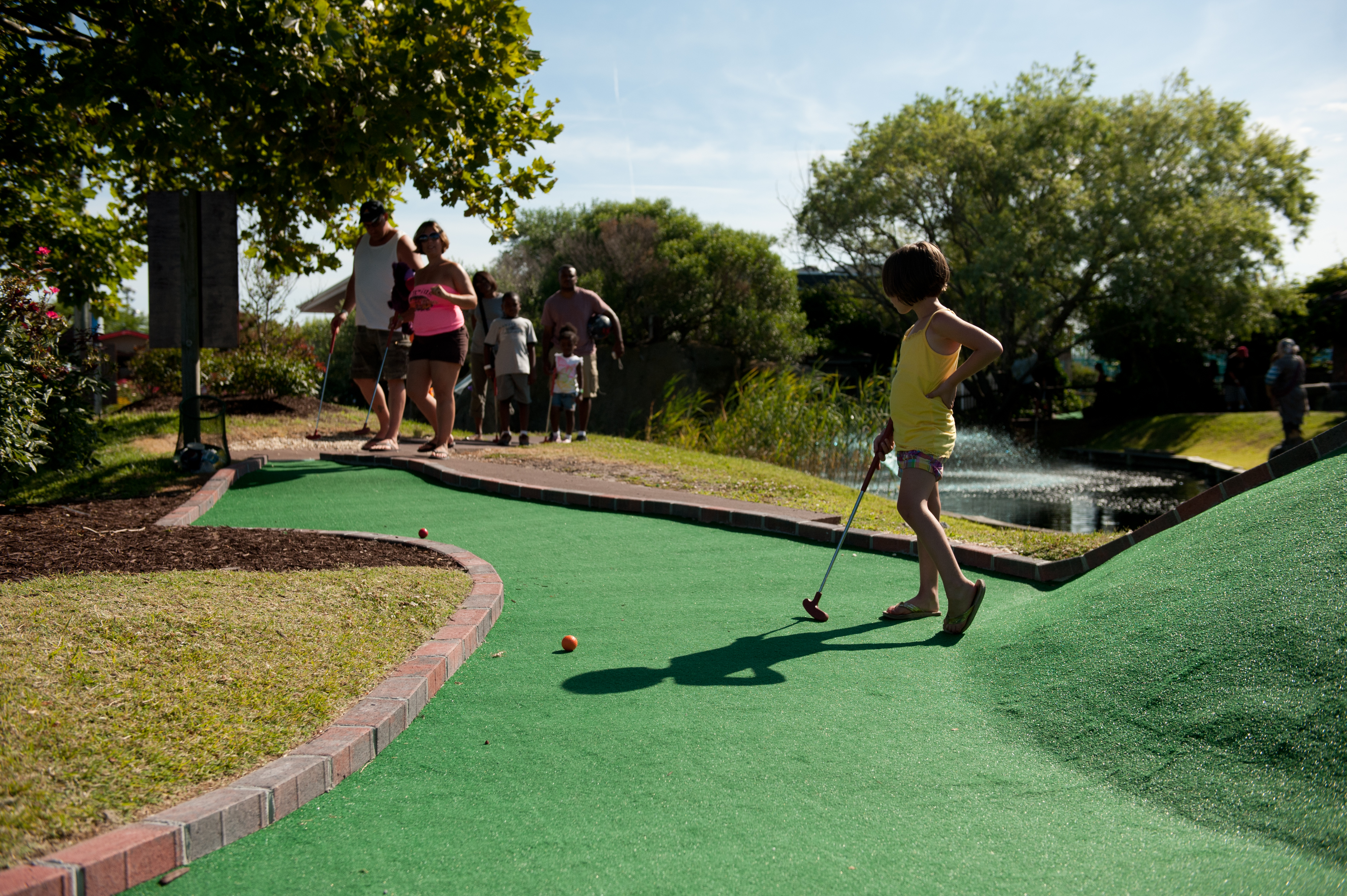 jolly-rogers-mini-golf-family-of-three a young girl with short dark hair playing miniature golf with her parents