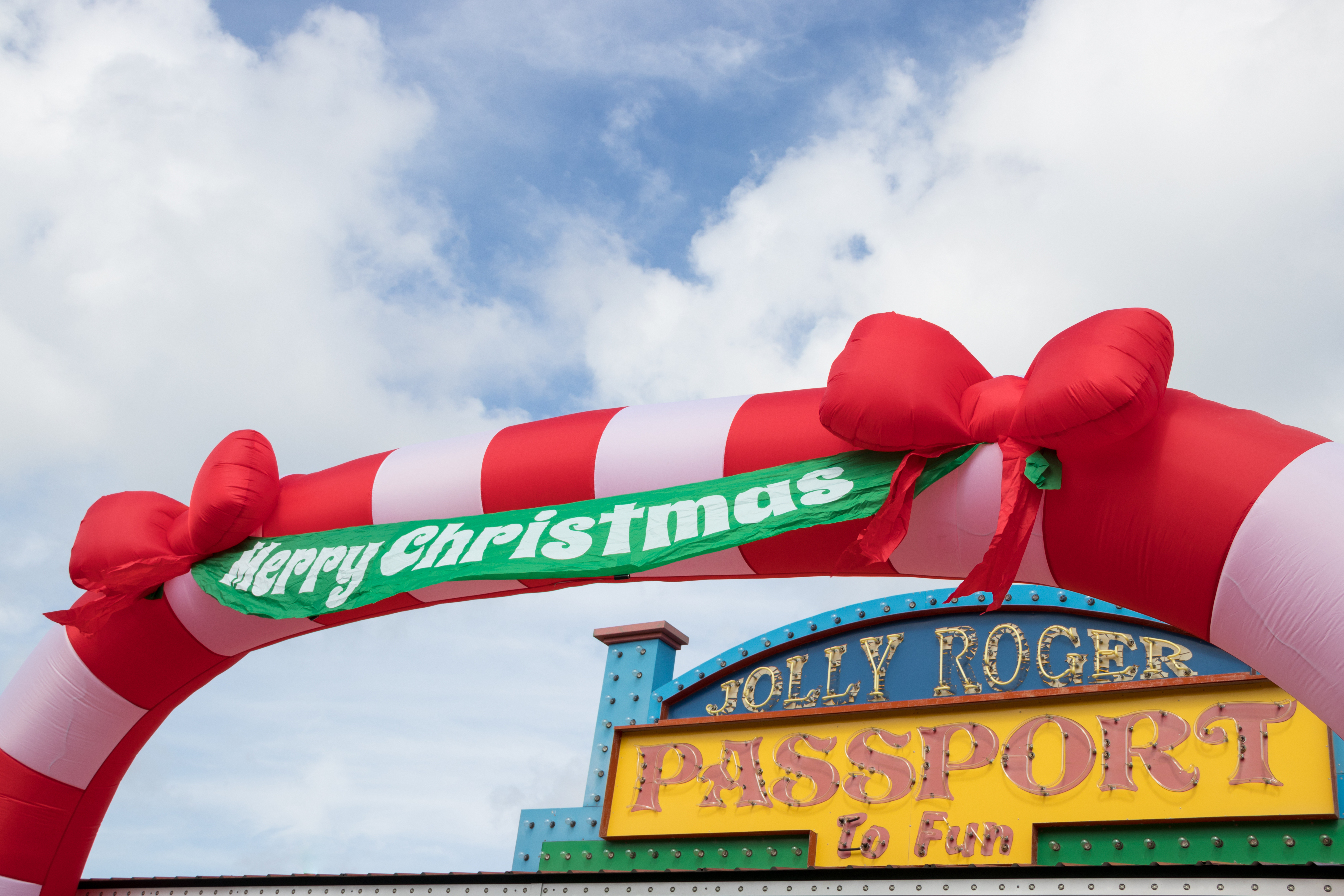 Red and White Christmas Blow Up Arch on top of Jolly Roger Passport to Fun Sign