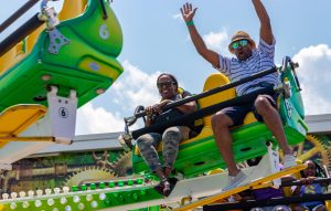 two people on a green carnival ride, one with their hands in the air, smiling.